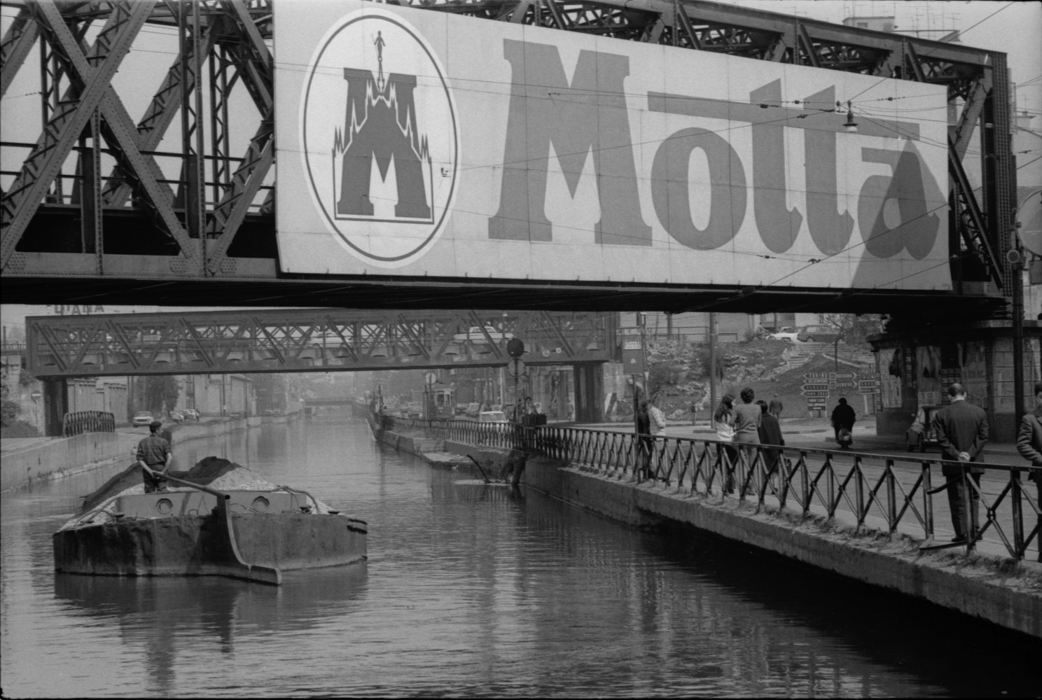 Toni Nicolini, Uomo trasporta della ghiaia sul barcùn, la tradizionale chiatta milanese, lungo il Naviglio Grande a Milano, Milano, 1970