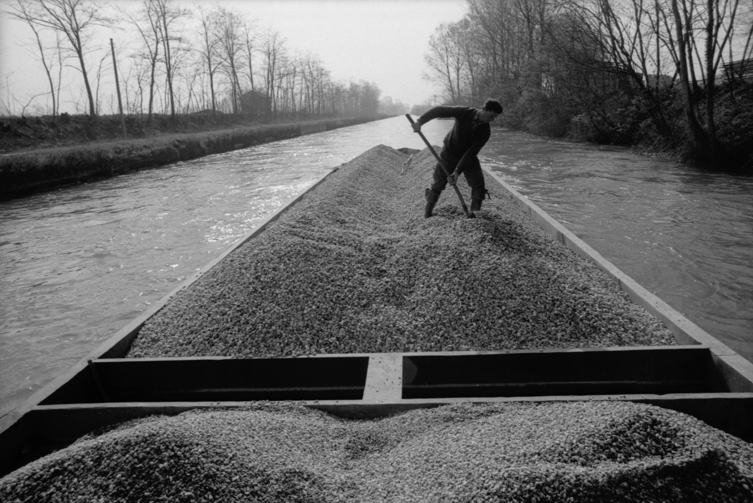 Toni Nicolini, Uomo trasporta della ghiaia sul barcùn, la tradizionale chiatta milanese, lungo il Naviglio Grande, Milano, 1970